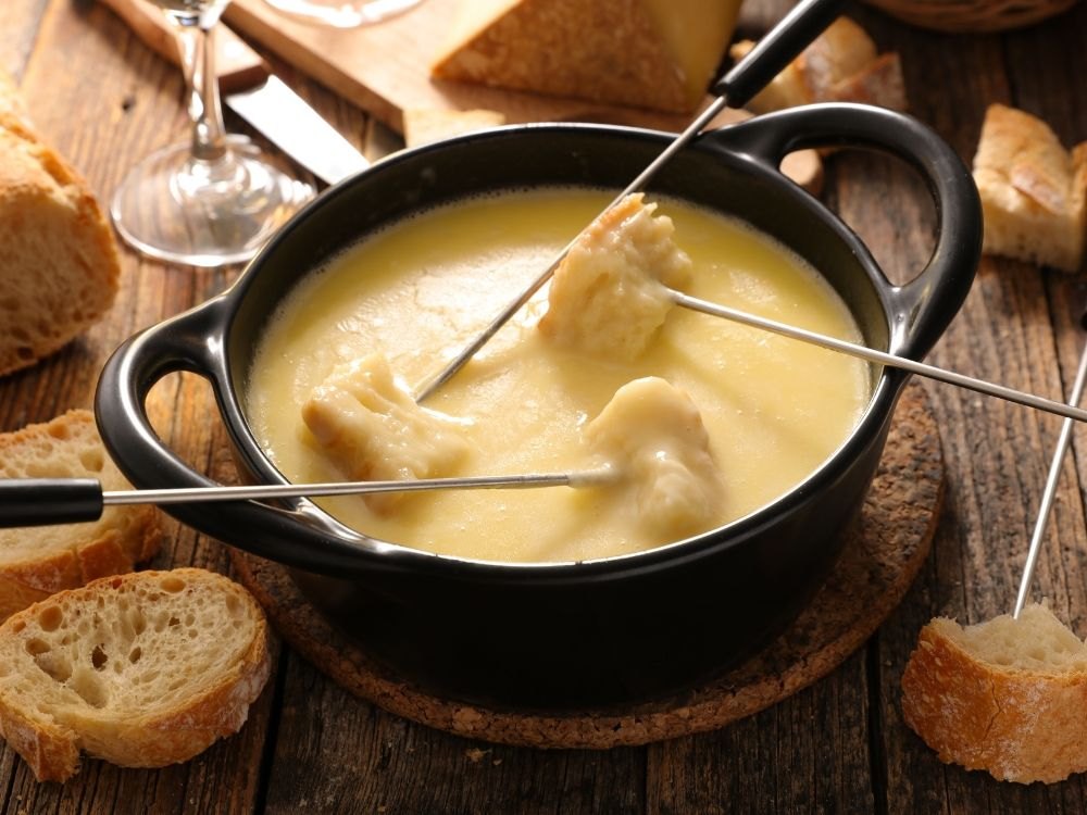 Kaasfondue in een zwarte pan, met stukjes stokbrood aan fonduevorken